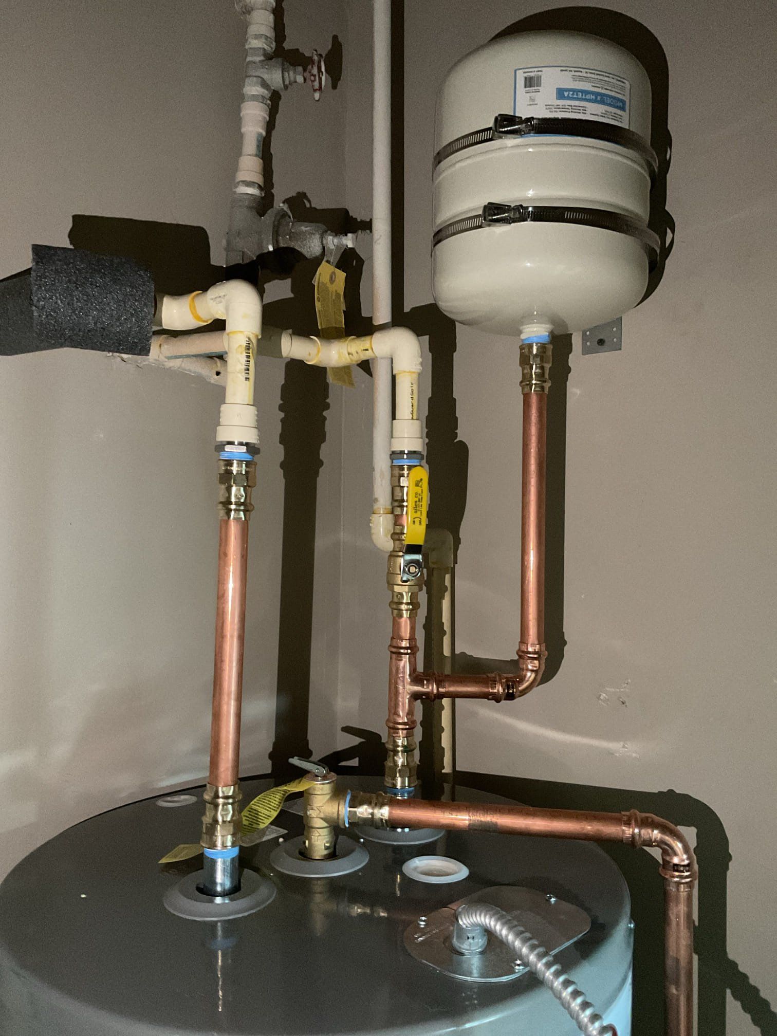 Water heater with copper pipes and a white expansion tank in a utility room.
