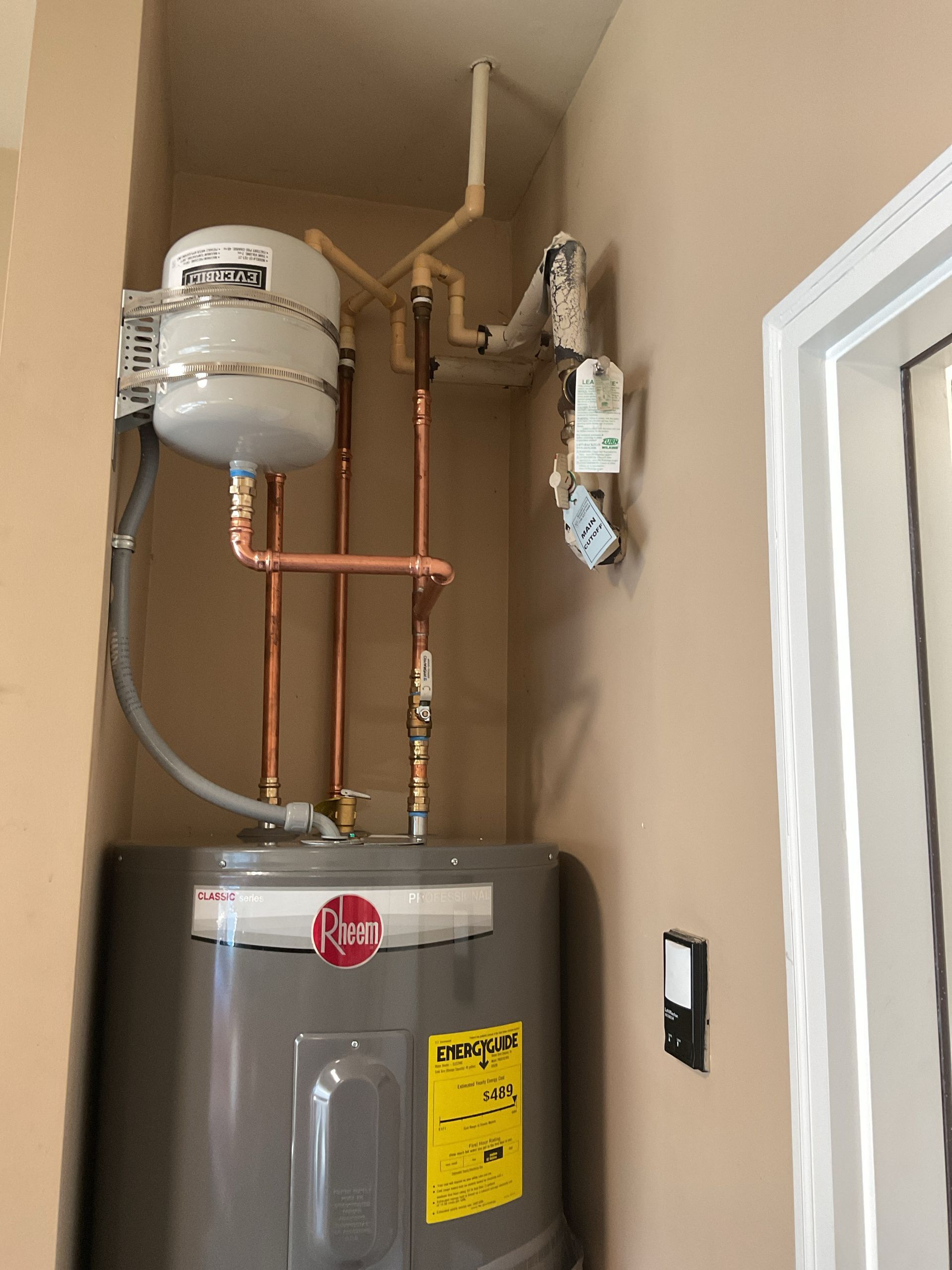 Water heater with copper pipes and expansion tank in a utility closet.