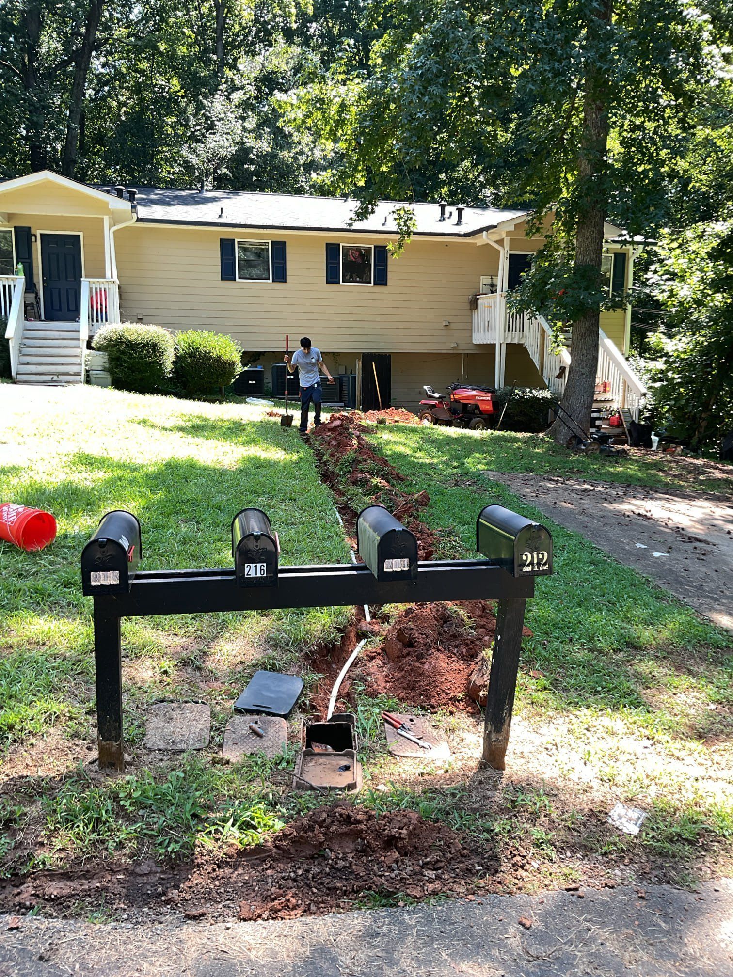 Mailboxes near a duplex; a person works on landscaping in front of the building.