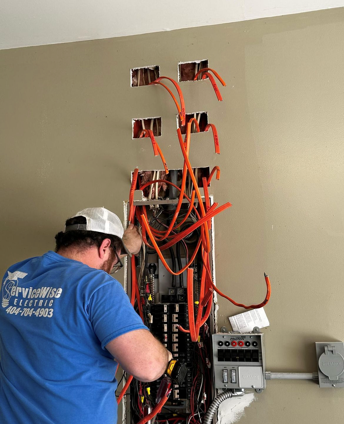 Electrician working on a panel with orange wires exposed in a wall.