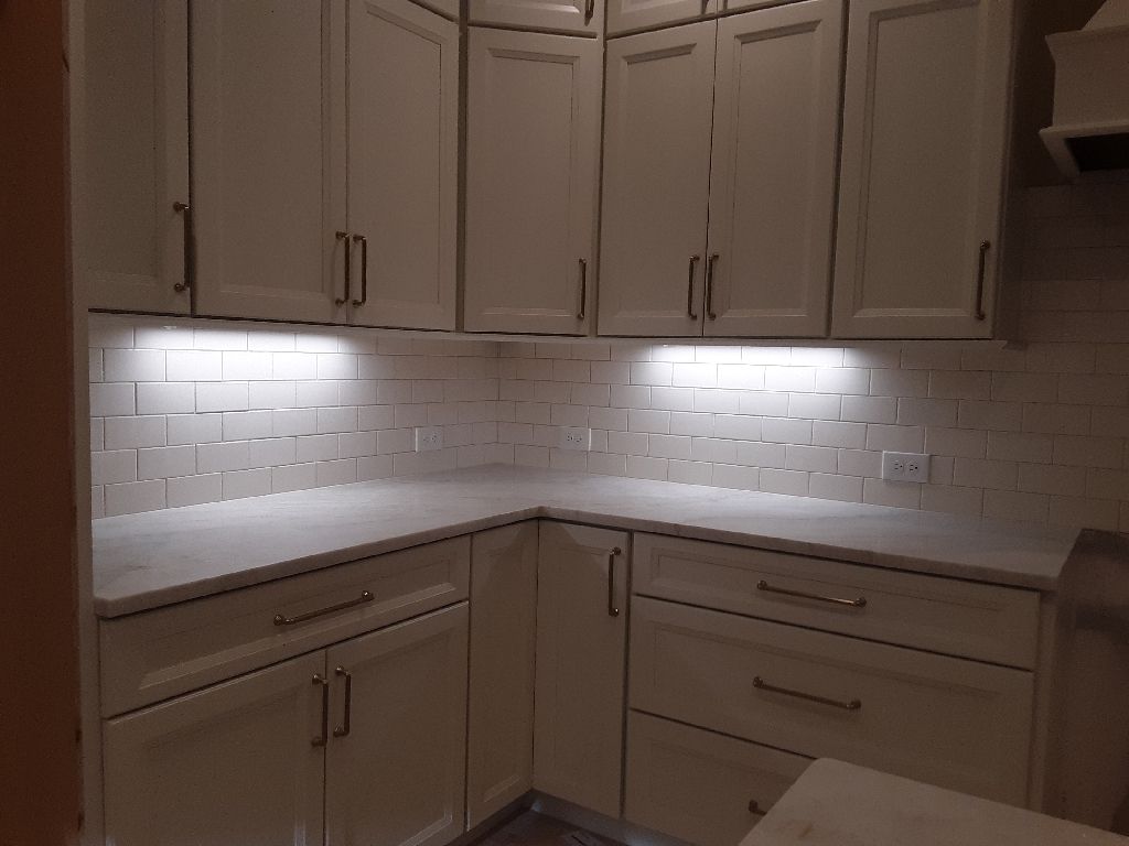 White kitchen cabinets with countertop and backsplash, under-cabinet lighting.