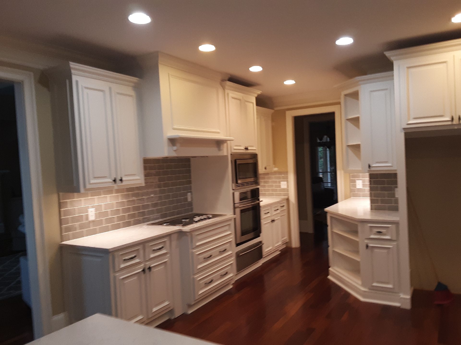 Cream-colored kitchen with white countertops and cabinetry. Brown hardwood floors and a tile backsplash.