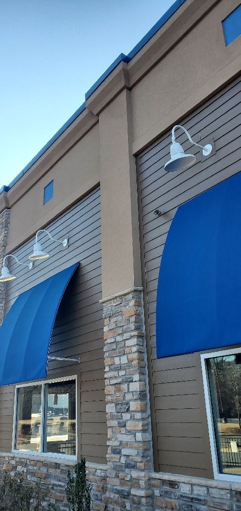 Exterior of a building with blue awnings, stone columns, and wall-mounted lights.