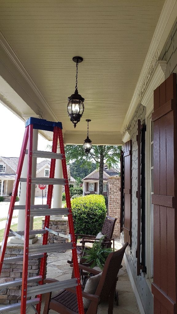 A red ladder beneath a porch ceiling, with two hanging black lanterns.
