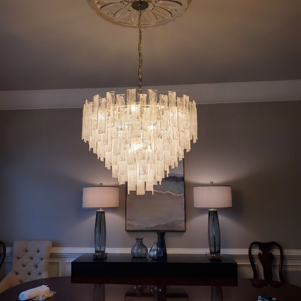 A dining room with a large, elaborate chandelier. Two lamps flank a dark console table with a painting above.