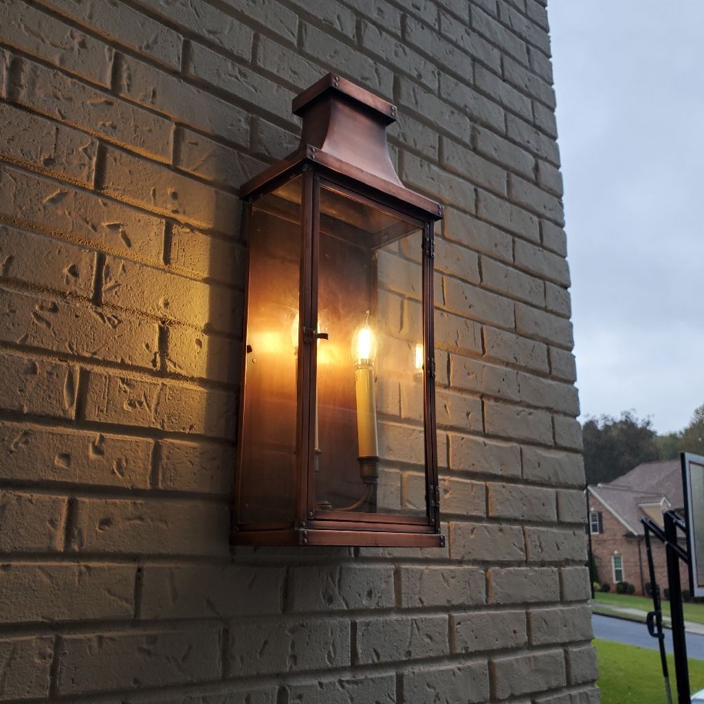 Copper lantern on a brick wall, lit with candles, outdoors.