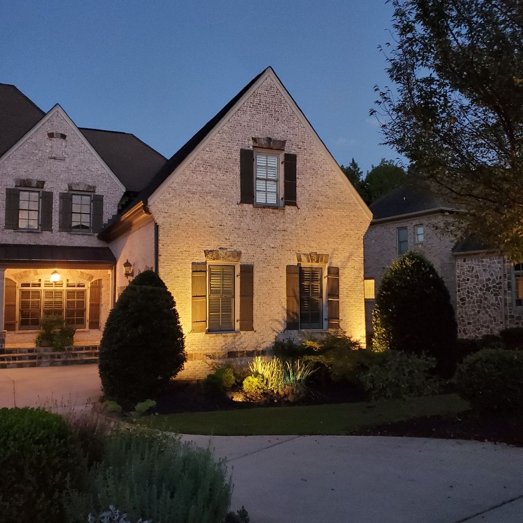 A brick house illuminated at dusk, with landscaping and a curved driveway.
