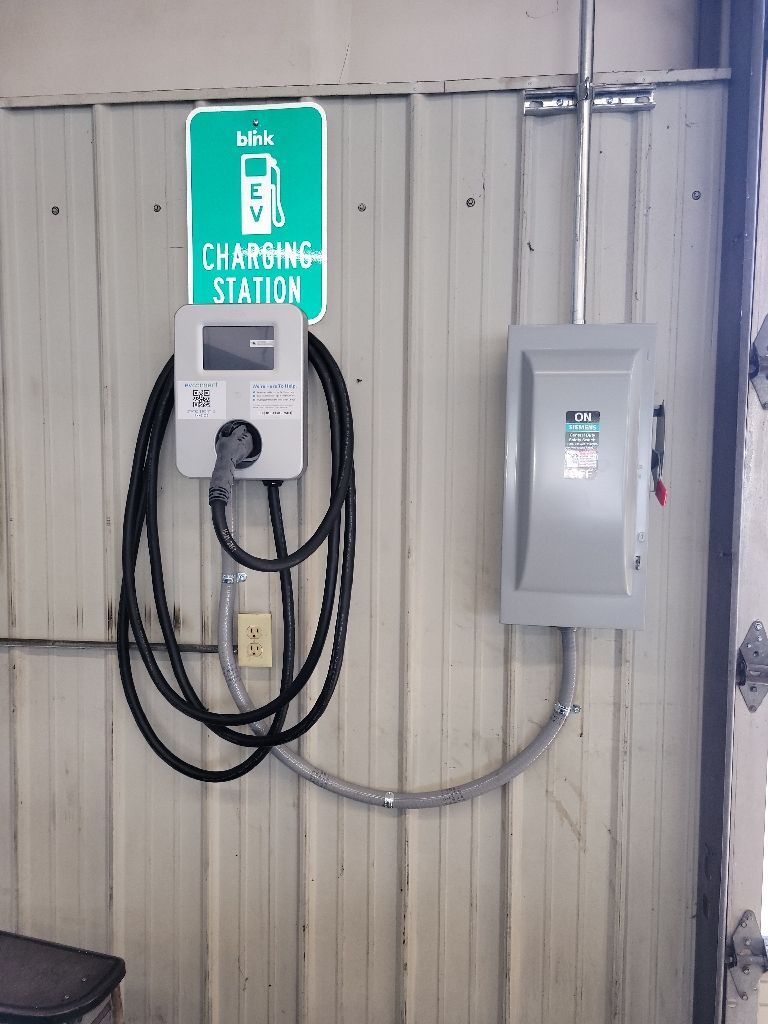 Electric vehicle charging station on a wall with a sign and electrical box.