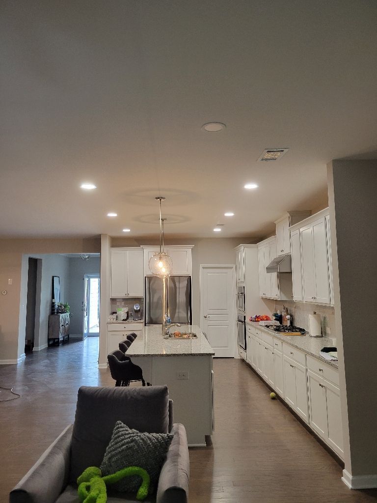 Modern kitchen with white cabinets, island, and stainless steel appliances. Hardwood floors and recessed lighting.