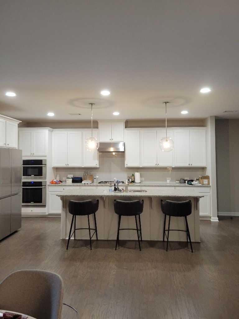 White kitchen with island, stools, stainless appliances, and pendant lights.