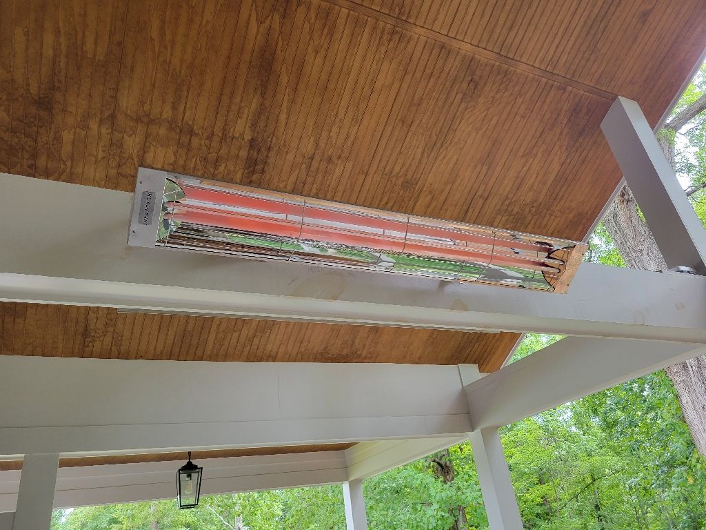 Infrared patio heater mounted on a brown wooden ceiling, under a white-painted porch roof.