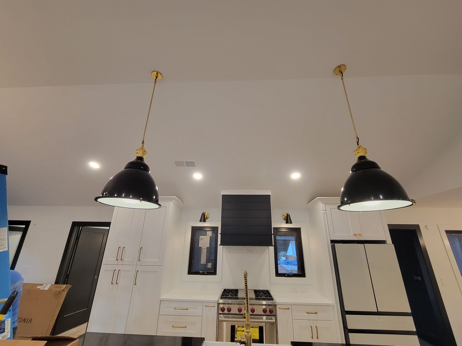 Two black pendant lights hanging above a kitchen island with white cabinets and a black range hood.