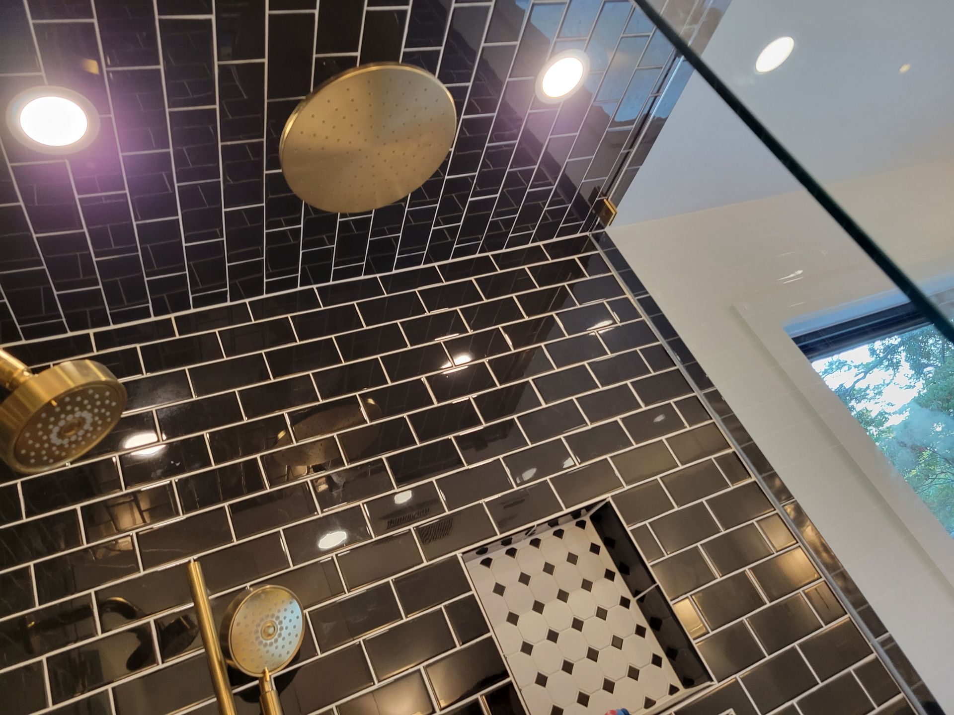 Black tiled shower with gold fixtures and overhead rain showerhead.