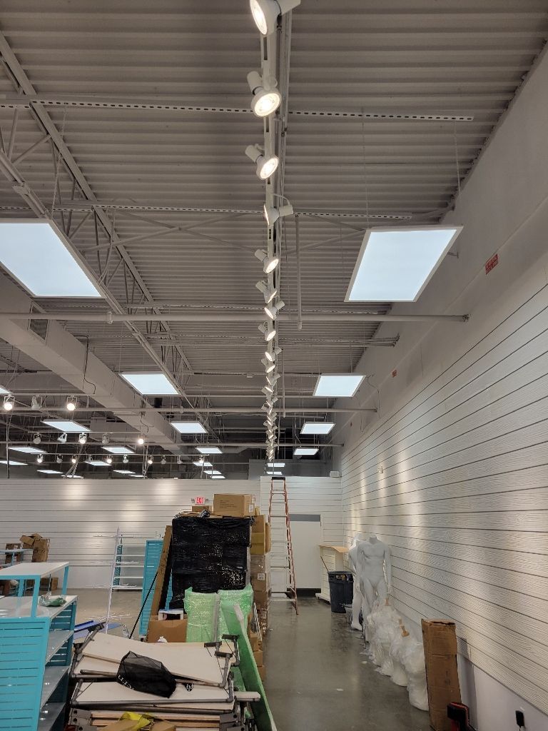 Interior of a store under construction with overhead track lighting and a partially built wall.