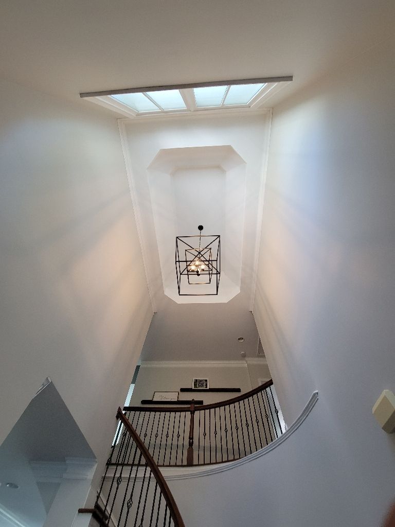 Stairwell with a skylight, chandelier, and a curved wooden banister. The walls are white.