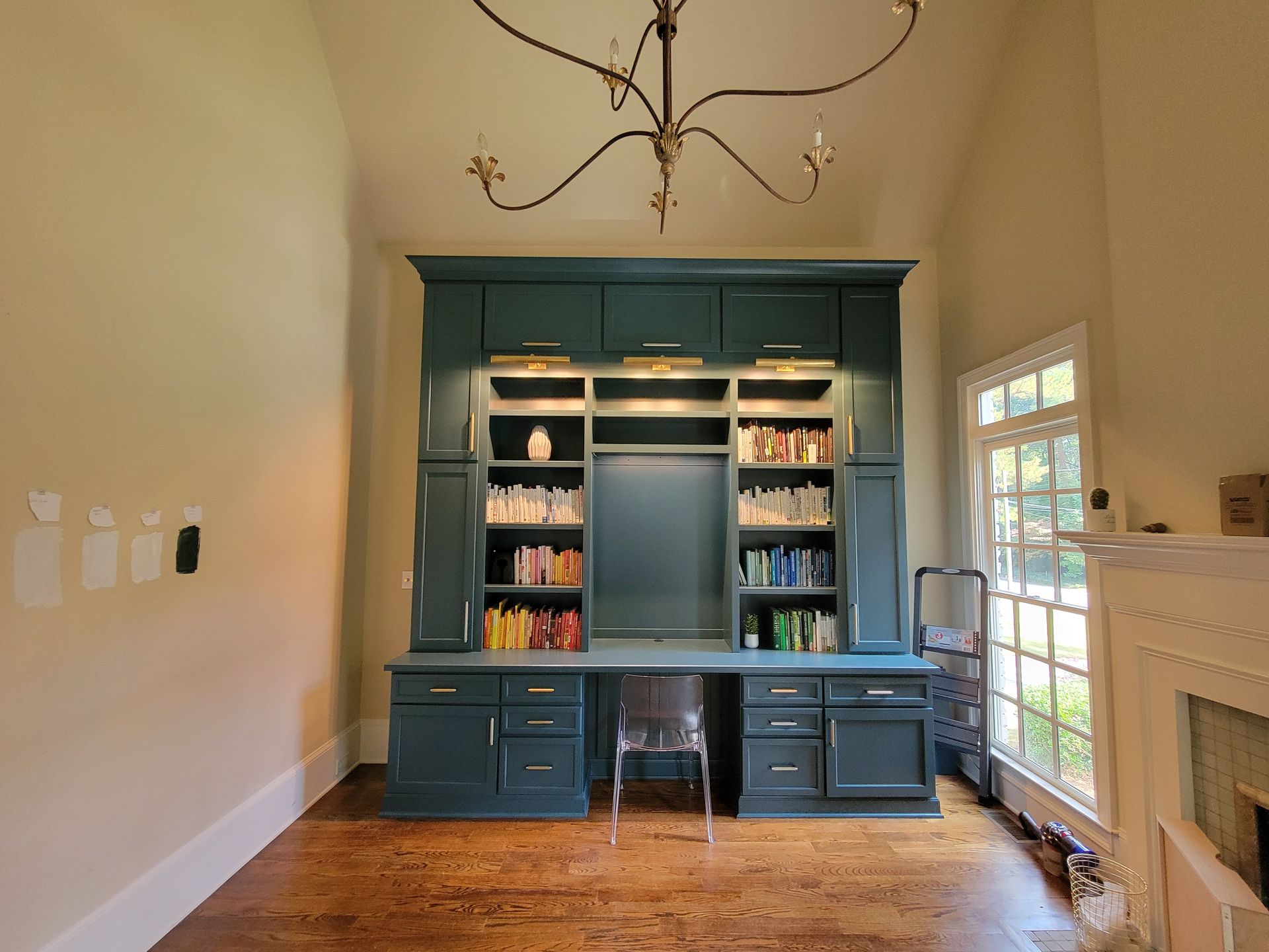 Built-in teal-painted desk and storage unit, with shelves, and overhead lighting.  Room with window, fireplace, and hardwood floors.