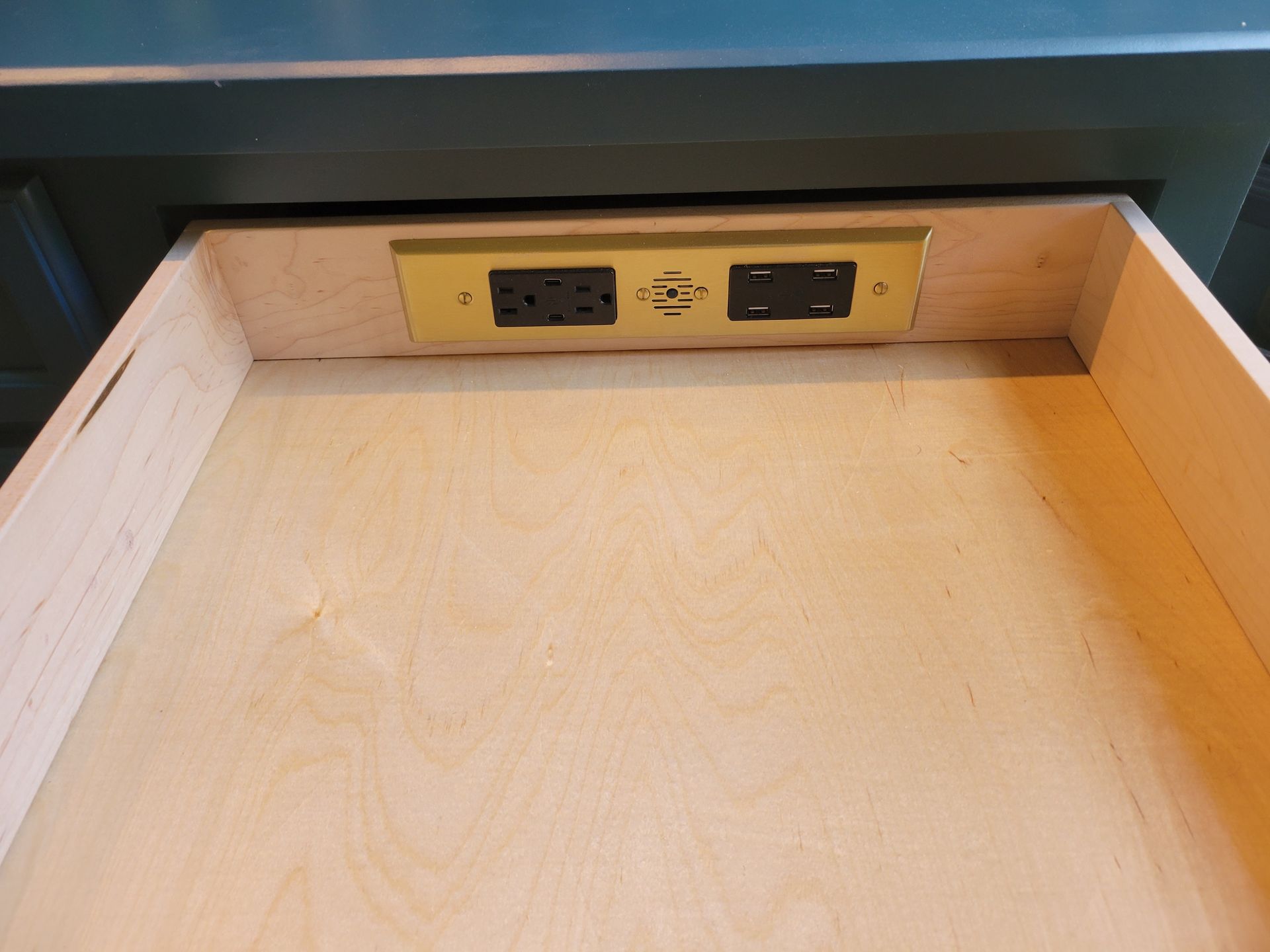Open wooden drawer with electrical outlets and USB ports in a gold-colored plate.