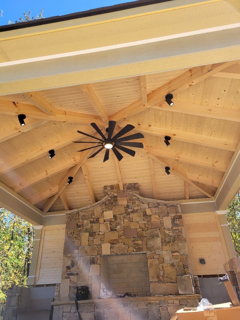 Outdoor pavilion with stone fireplace, wood ceiling, and black fan.