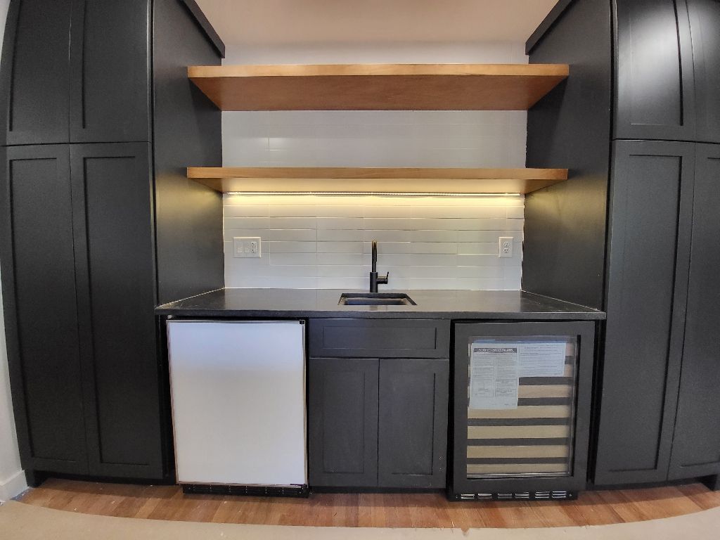 Dark gray home bar with fridge, wine cooler, and wooden shelves.