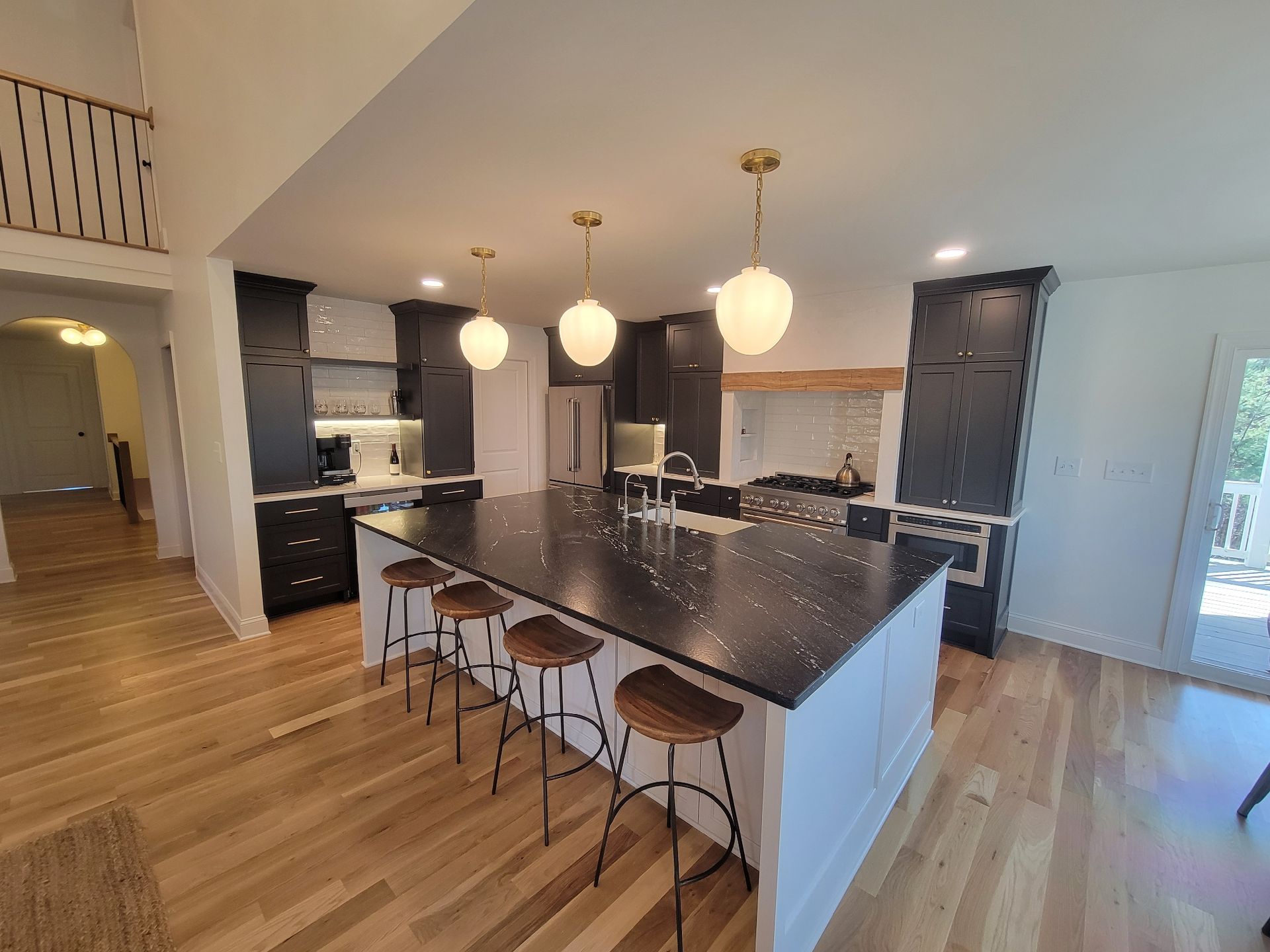 Modern kitchen with large black island, white cabinets, gold pendant lights, and wood floors.