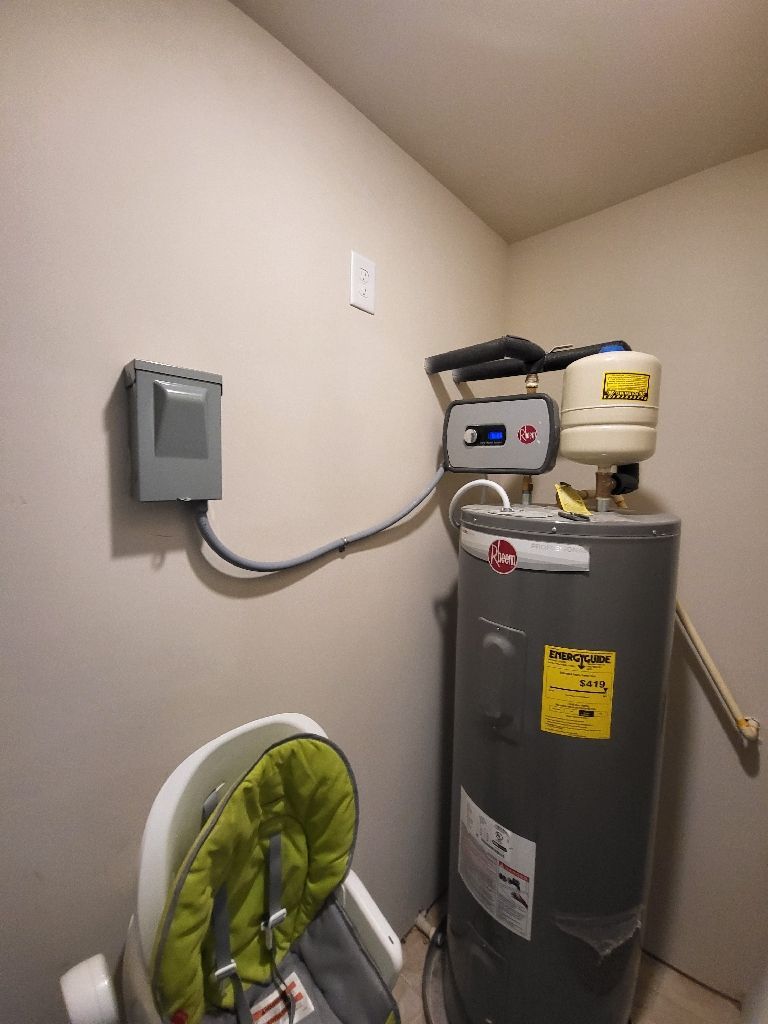 Water heater in a corner next to a high chair, conduit runs to electrical box on wall.
