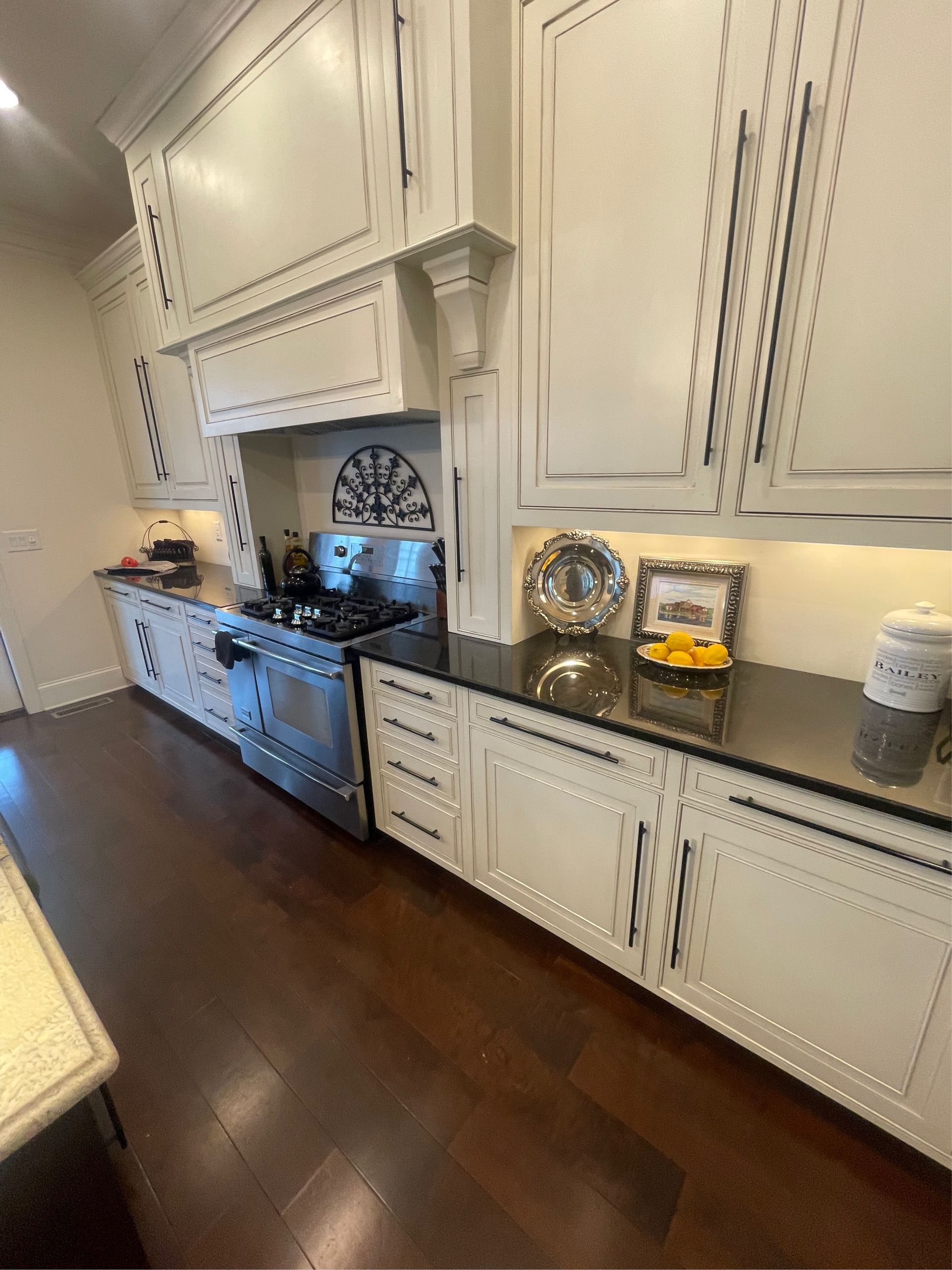 Kitchen with white cabinets, black countertops, stainless steel appliances, and dark wood floors.