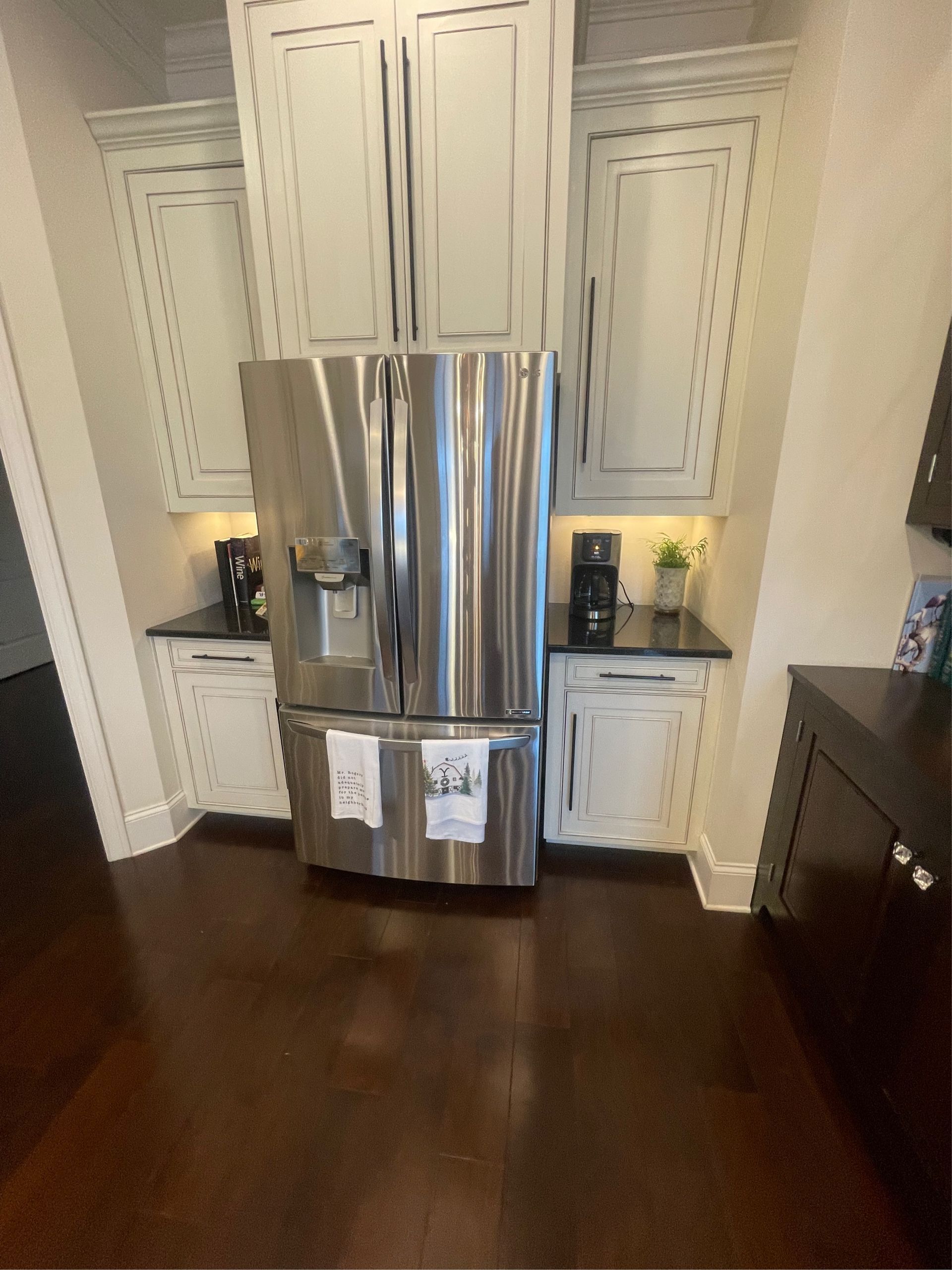 Stainless steel refrigerator in a kitchen with white cabinets and dark hardwood floors.