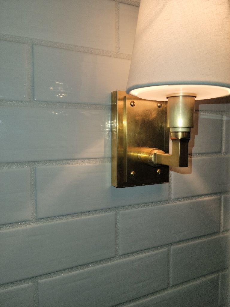 Brass sconce with white lampshade on white subway tile.