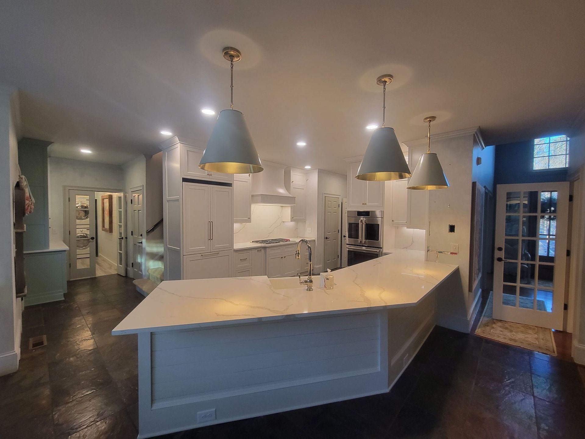Modern white kitchen with island, pendant lights, and dark wood floors.