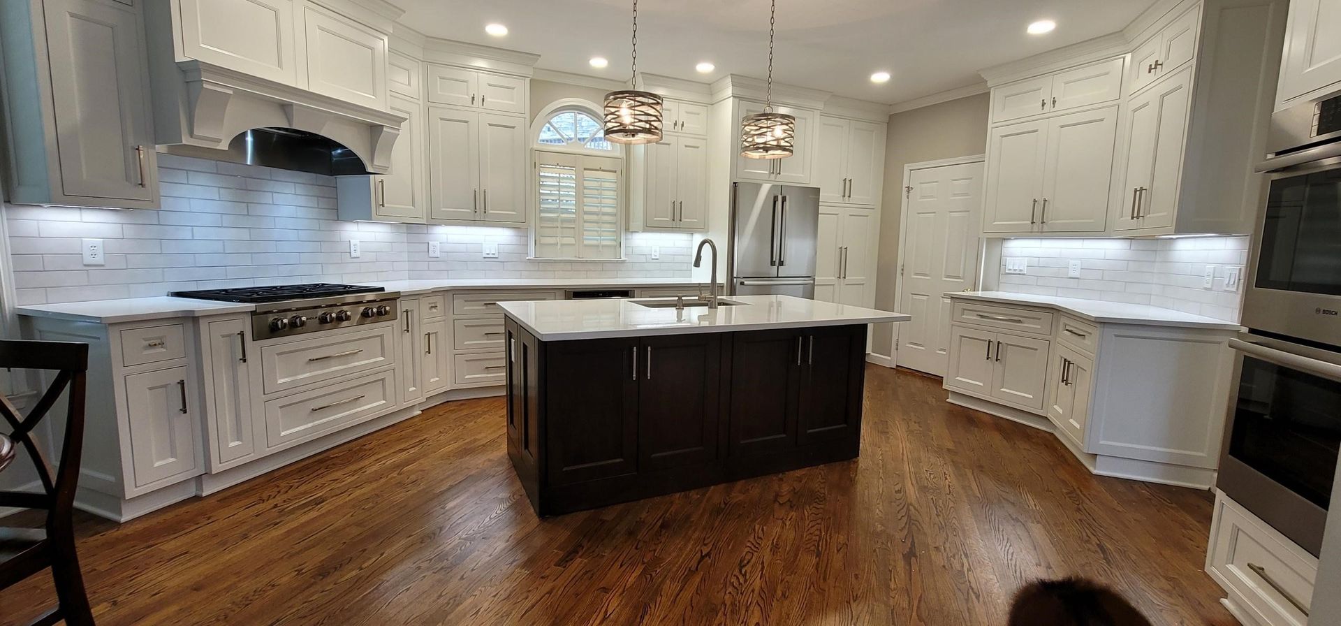 A spacious kitchen with white cabinetry, a dark island, and a hardwood floor.