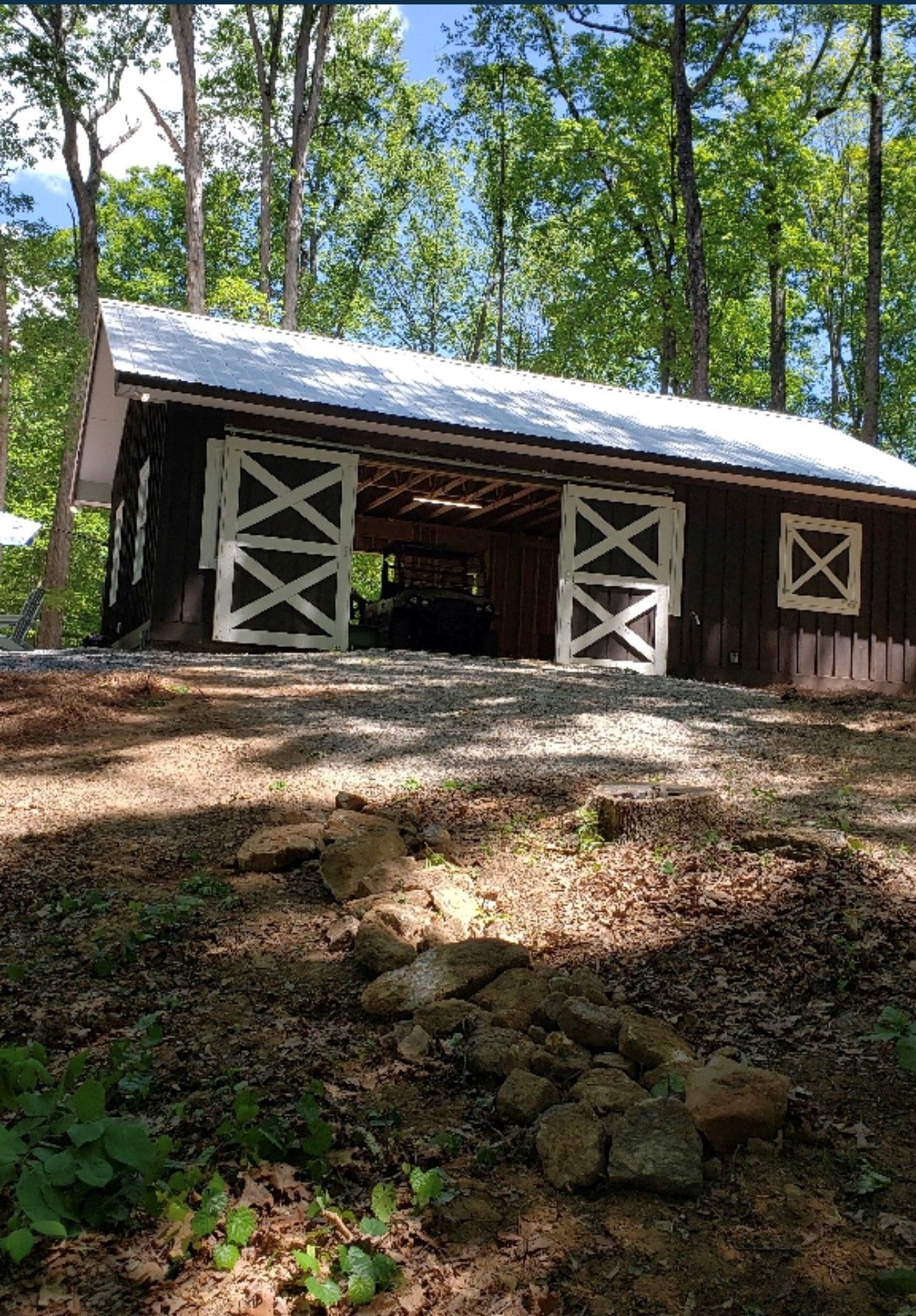 Barn with white sliding doors, brown siding, and a tin roof, set in a wooded area.