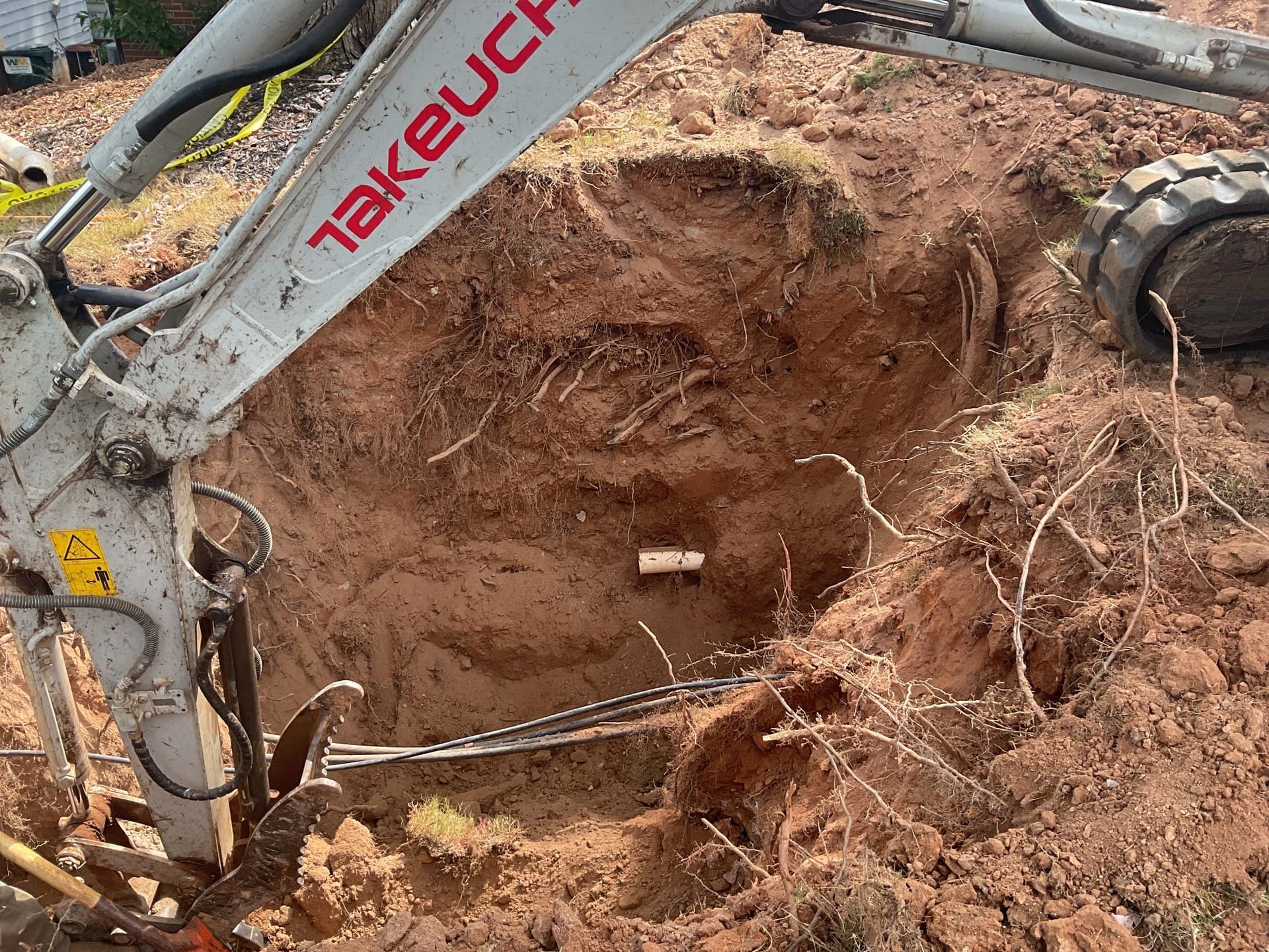 A small excavator digs into red soil, revealing a buried pipe.