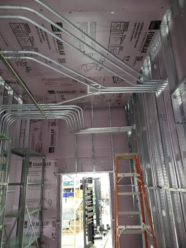 Interior construction with metal studs, electrical conduit, pink insulation, and a ladder.