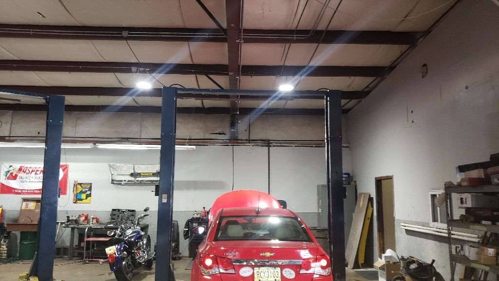 Red car on a lift inside a garage, with a motorcycle and tools in the background.