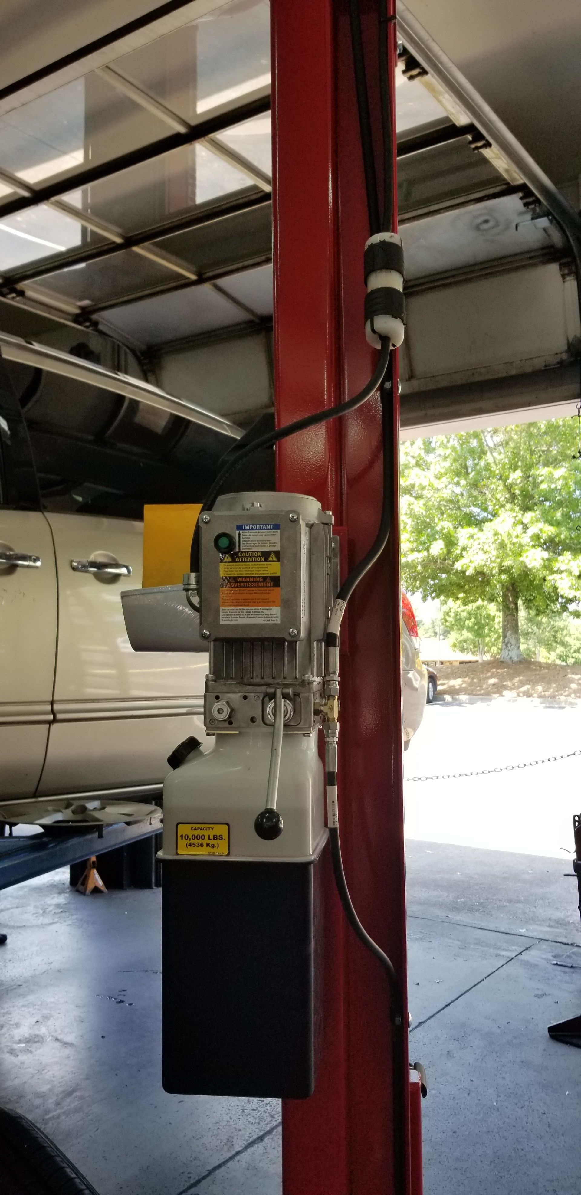 Red car lift post with a hydraulic pump system attached. A car is partially visible behind the lift.