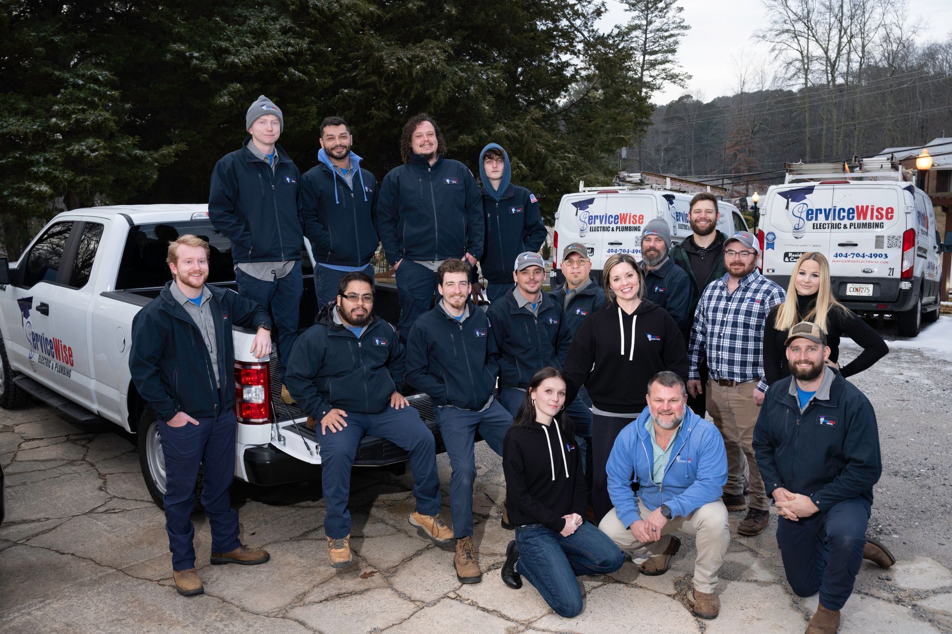 Group of people wearing blue jackets posing near a white truck and vans.