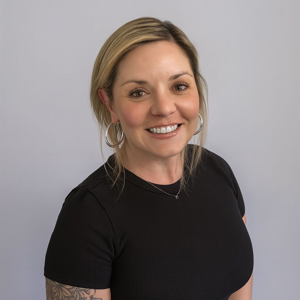 Woman with blonde hair wearing a black shirt, smiling, hoop earrings, and a tattoo on her arm.