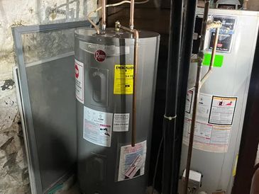 A water heater is sitting in a basement next to a window.