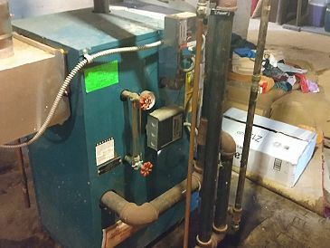 A blue boiler is sitting in a basement next to pipes.