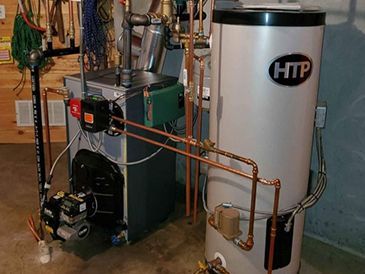 A htp water heater is sitting next to a boiler in a basement