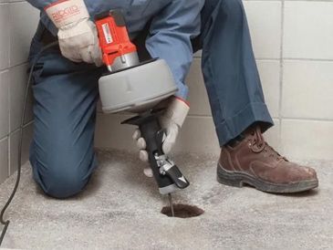 A man is using a drain cleaner to clean a hole in the floor.