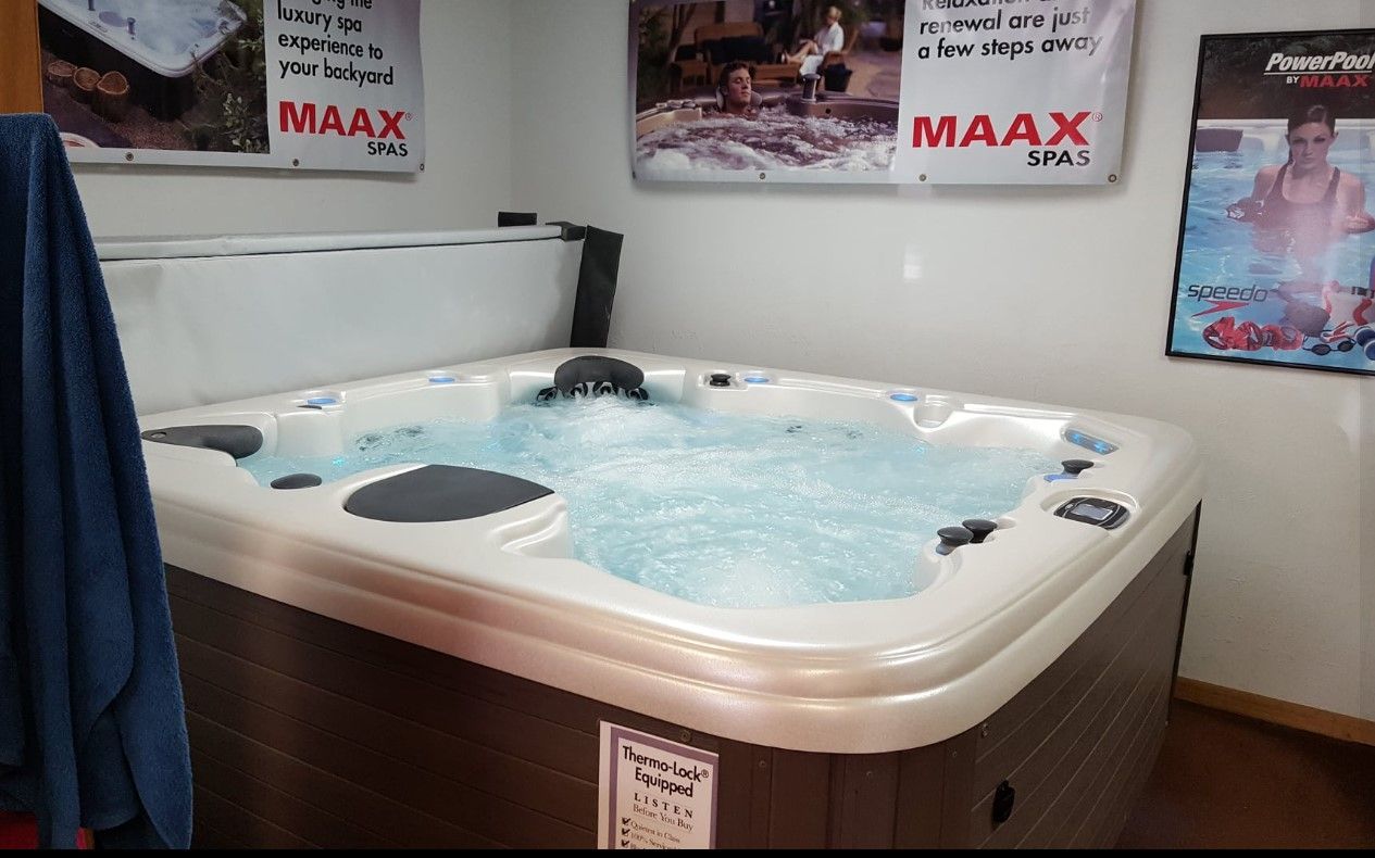 Hot tub with bubbling water; dark brown cabinet; white trim; MAAX sign in the background.