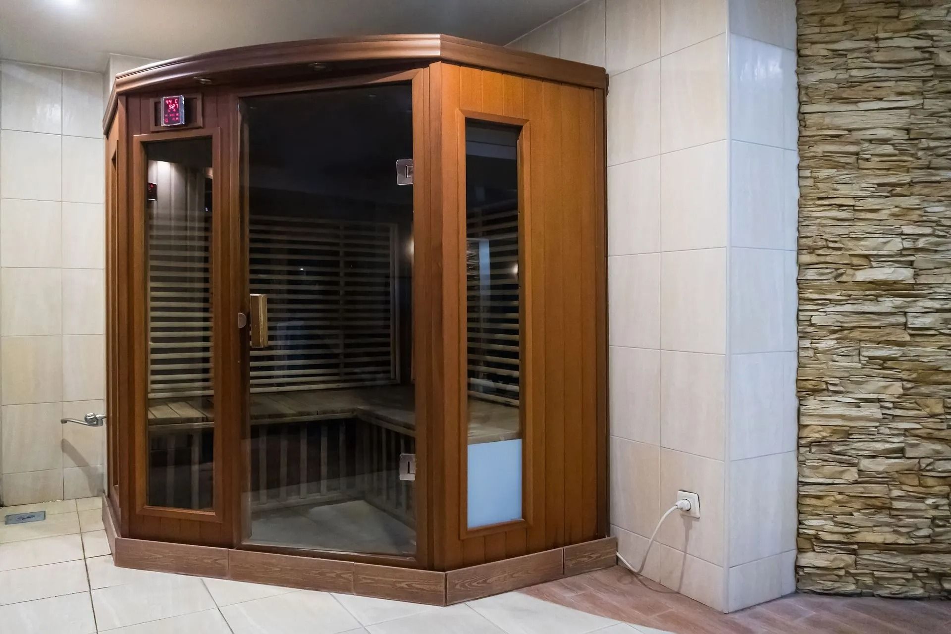 Wooden sauna with glass door and windows, set against stone and tile walls.