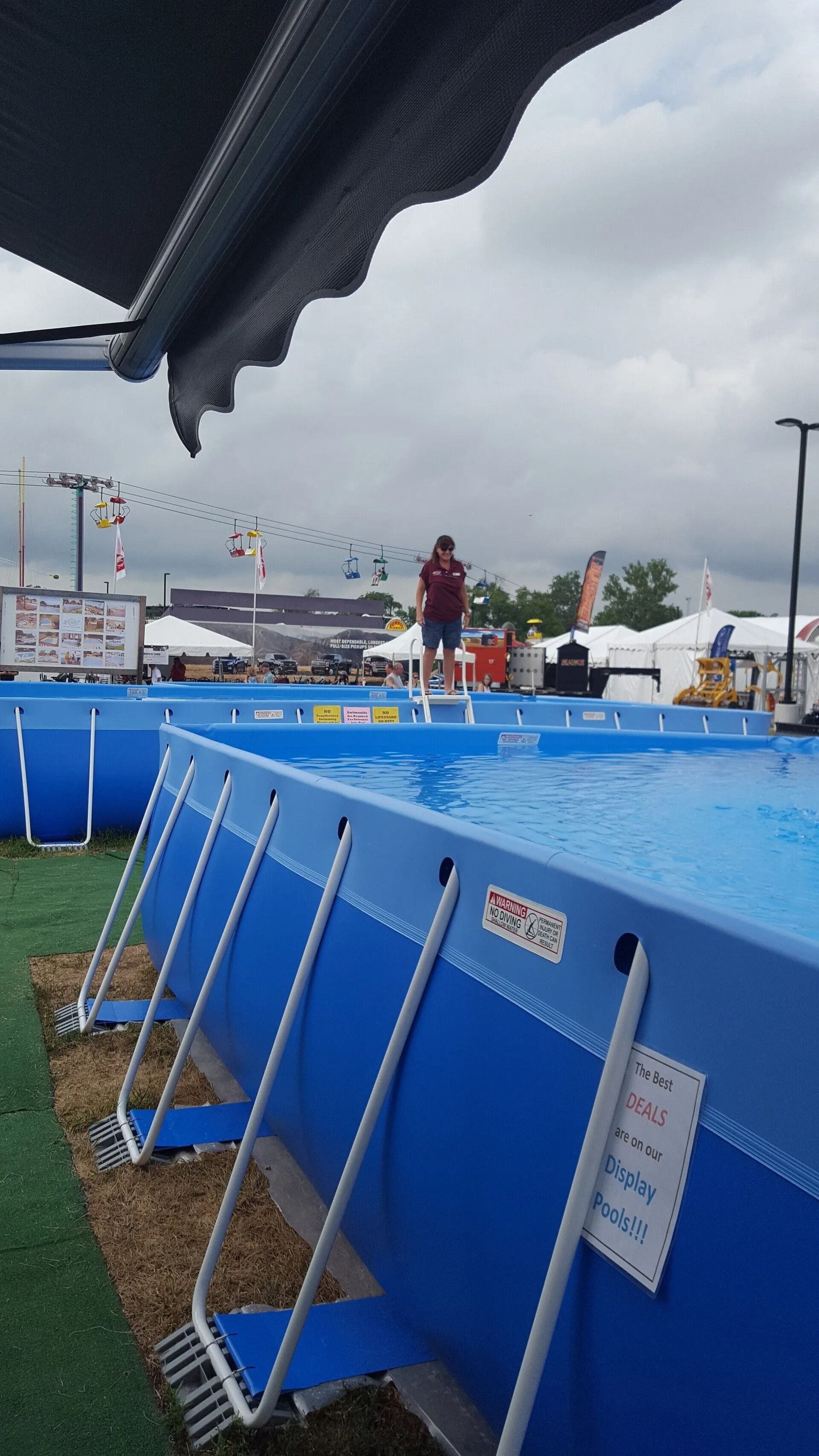 Person standing at edge of a blue rectangular pool, likely at an outdoor event.