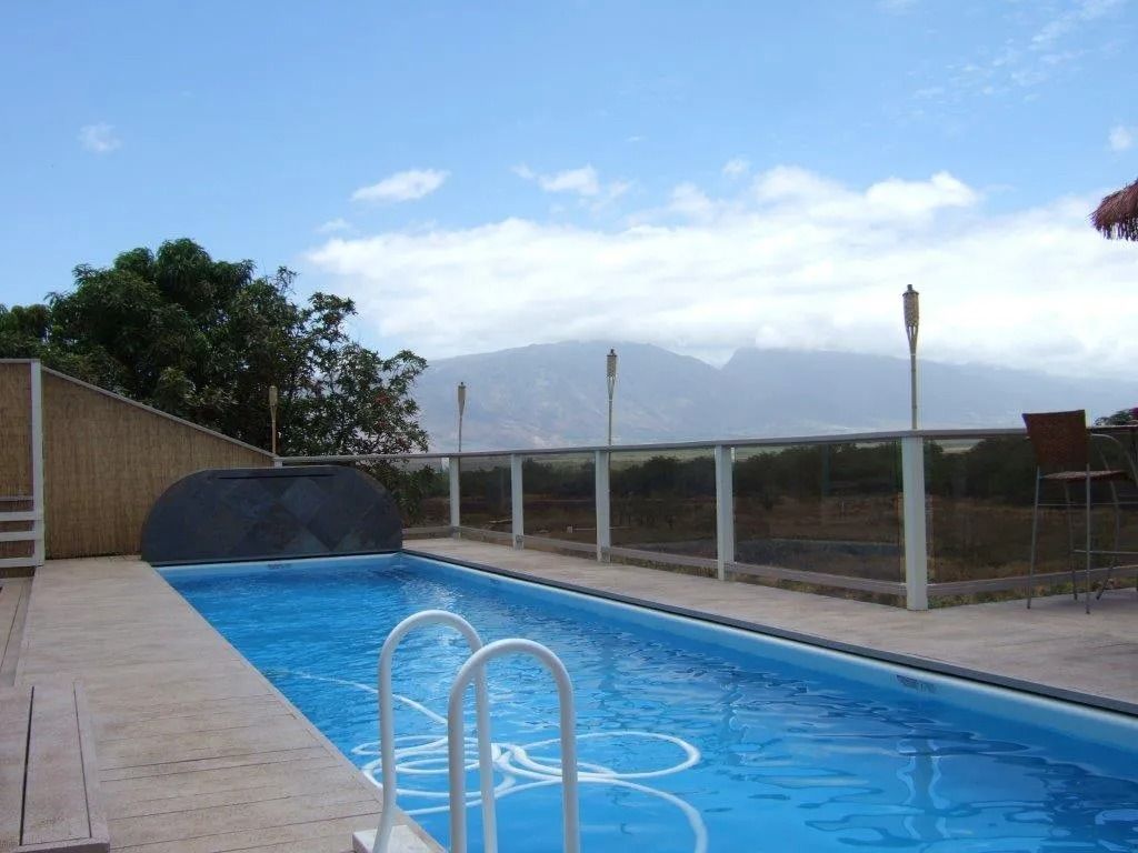 Long, blue swimming pool with mountain view under a partly cloudy sky.