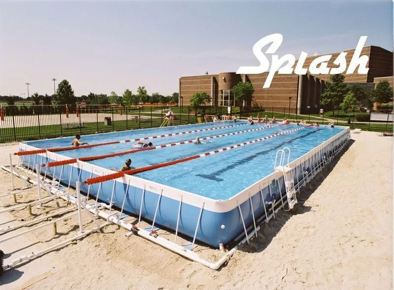 Blue rectangular above-ground pool with lane markers, people swimming. Exterior shot, sunny day. Building in background, word 