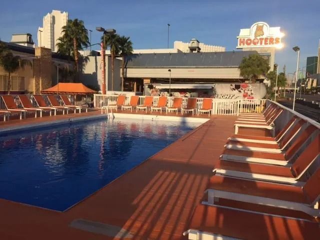 Poolside scene at Hooters. Orange lounge chairs by a pool with the Hooters restaurant in the background.