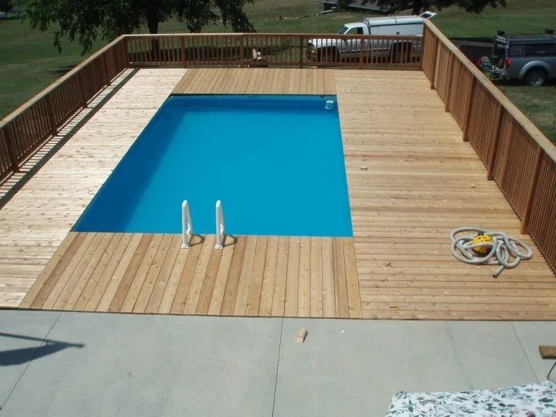 A rectangular pool surrounded by a wooden deck and railing. Blue water, brown wood. Outdoors.