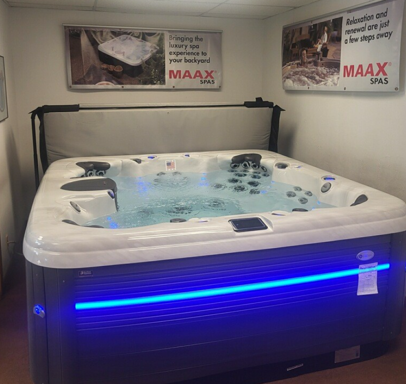 A lighted MAAX spa in a showroom with advertising.
