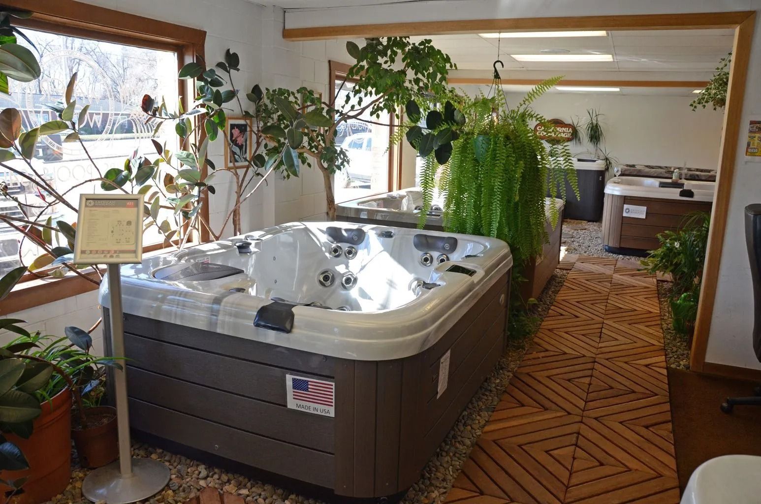 Hot tub display room with a large, brown and white hot tub surrounded by plants.